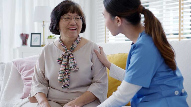 Adult child and older parent reviewing medications and a home safety checklist at a kitchen table.